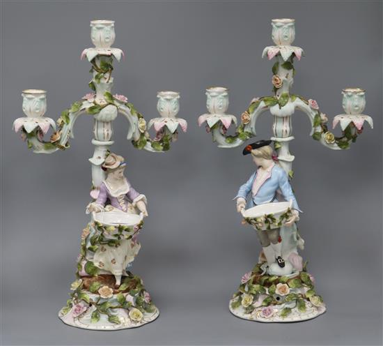 A pair of German three light table candelabra, modelled with a figure of a gallant and lady holding baskets of flowers, height 42cm